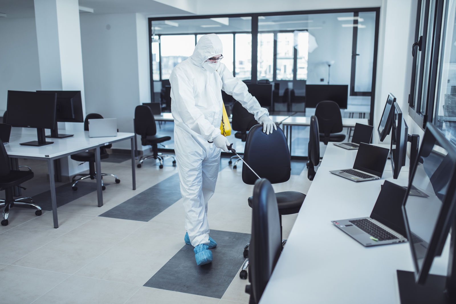 Fachkraft in Schutzkleidung führt eine Flächendesinfektion in Praxisräumen durch