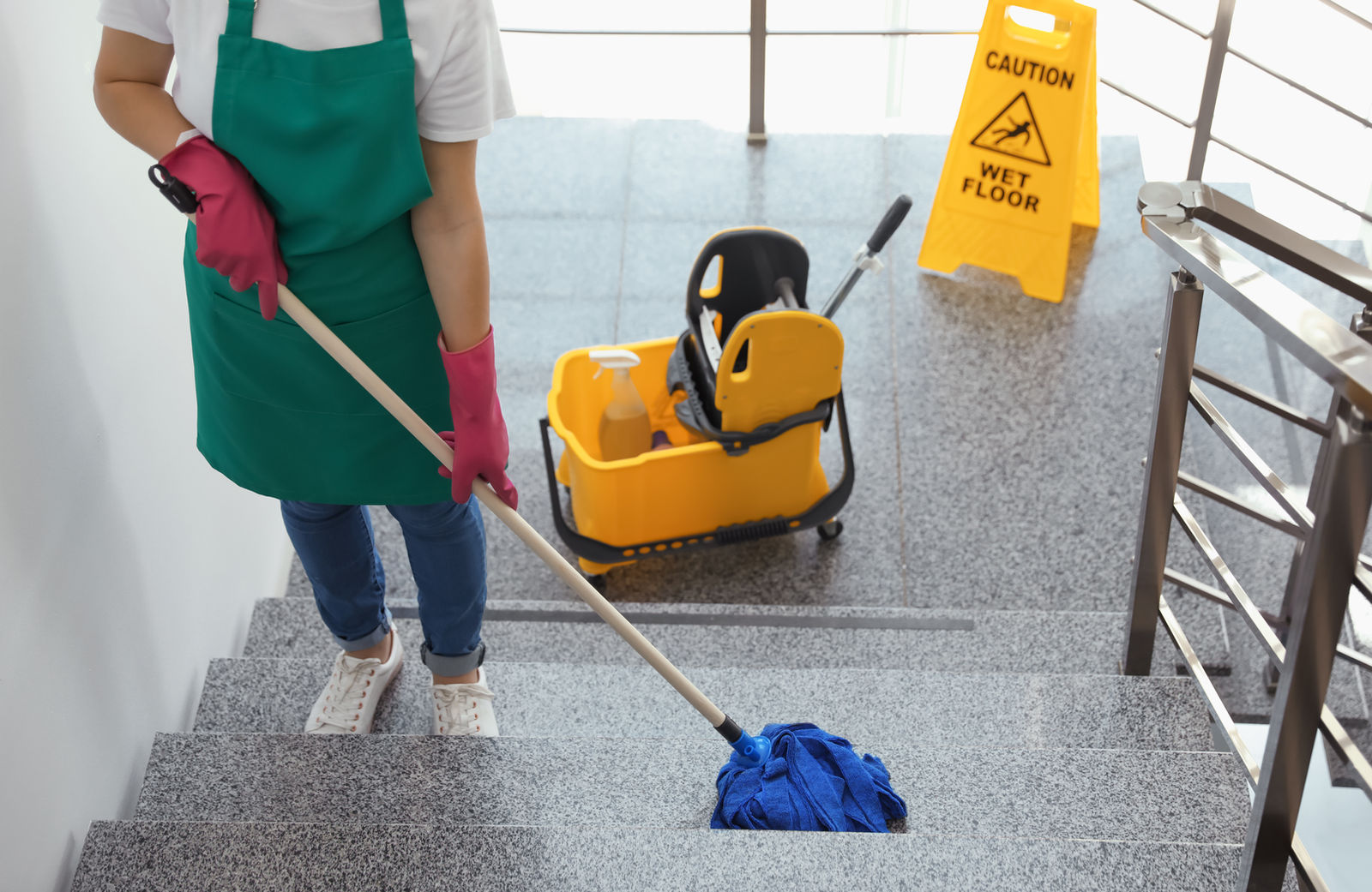 Treppenhausreinigung: Stufen werden gewischt, daneben ein gelbes Warnschild
